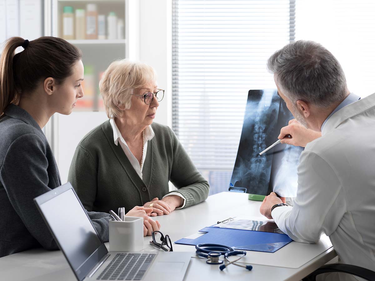 Doctor explaining bone density test results to a senior woman and her caregiver, raising awareness on osteoporosis and bone health